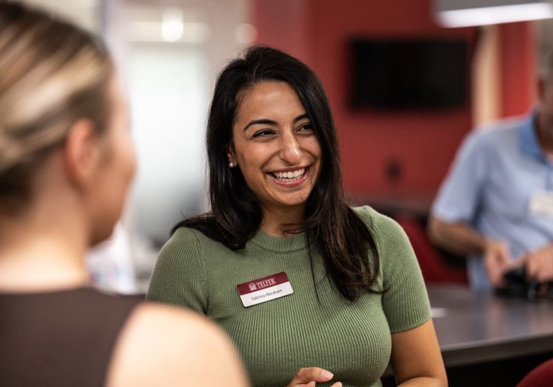 A woman in a green shirt smiles while in conversation with another person