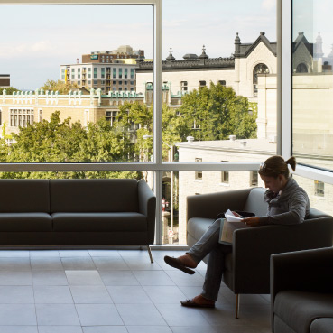 Une étudiante de Telfer installée dans un divan, devant de grandes fenêtres qui offrent une belle vue sur le campus.